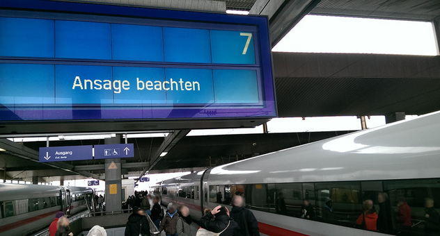 "Ansage beachten" steht auf der Anzeigetafel des Bahnsteigs neben einem stehenden ICE. Bild: hamo