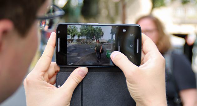 Ein Mann fotografiert mit seinem Smartphone mit etwas Entfernung eine Frau auf der Straße. Bild: checked4you