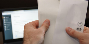 Ein Mann zieht eine Rechnung aus einem Umschlag, im Hintergrund steht ein Laptop. Bild: checked4you.de