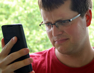 Ein junger Mann blickt skeptisch auf ein Smartphone, das er vor sich in der Hand hält. Foto: checked4you