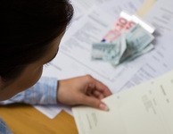 Frau mit Rechnung in der Hand, weitere und Geldscheine liegen vor ihr auf dem Tisch. (Foto: GinaSanders / Fotolia)
