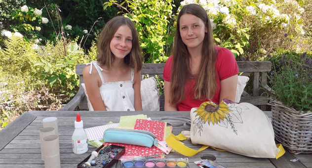 Zwei Mädchen sitzen nebeneinander an einem Gartentisch mit verschiedenen Bastelutensilien. Foto: Katja Goebel
