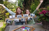 Zwei Mädchen heben ihre Arme hinter einem Brett mit mehreren Fotos, vor ihnen ein Tisch mit Bastelutensilien. (Foto: Goebel)