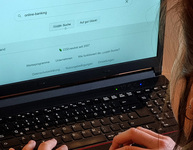Frau mit Laptop gibt "Online-Banking" in Suchmaschine ein. Foto: Verbraucherzentrale NRW