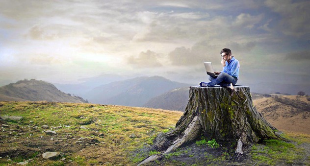 Mann sitzt auf einem Baumstamm in der Natur und schreibt am Computer (Bild: olly / fotolia.com)