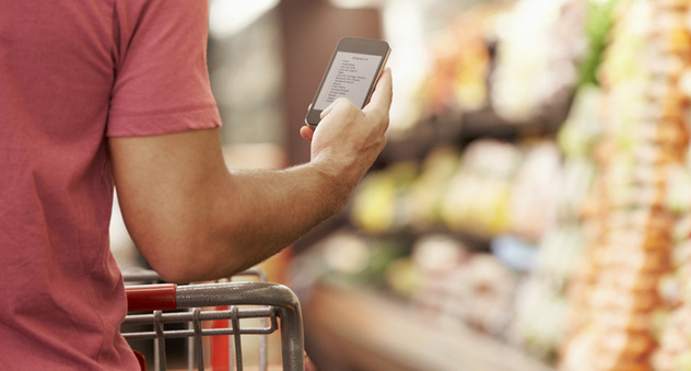 Mann guckt beim Einkaufen im Supermarkt auf ein Smartphone. Bild: Monkey Business/Fotolia.com