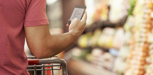 Mann guckt beim Einkaufen im Supermarkt auf ein Smartphone. Bild: Monkey Business/Fotolia.com
