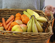Eine Frau trägt einen Weidenkorb mit Möhren, Äpfeln, Clementinen und Bananen. Foto: checked4you.de