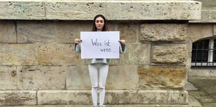 Eine junge schwarzhaarige Frau steht vor einer gemauerten Hauswand und hält eine Pappe mit der Aufschrift: "Was ist, wenn ..." in den Händen. Foto: checked4you