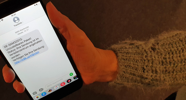 Smartphone in einer Hand zeigt betrügerische SMS von "TrackInfo". Bild: Verbraucherzentrale NRW
