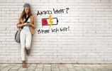 Junge Frau mit Smartphone lehnt an einer grauen Wand. (Bild: Verbraucherzentrale NRW)