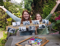 Zwei Mädchen heben ihre Arme hinter einem Brett mit mehreren Fotos, vor ihnen ein Tisch mit Bastelutensilien. (Foto: Goebel)