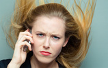 Frau mit Smartphone am Ohr, grimmigem Blick und nach oben fliegenden blonden Haaren. Foto: conorcrowe/Fotolia.com